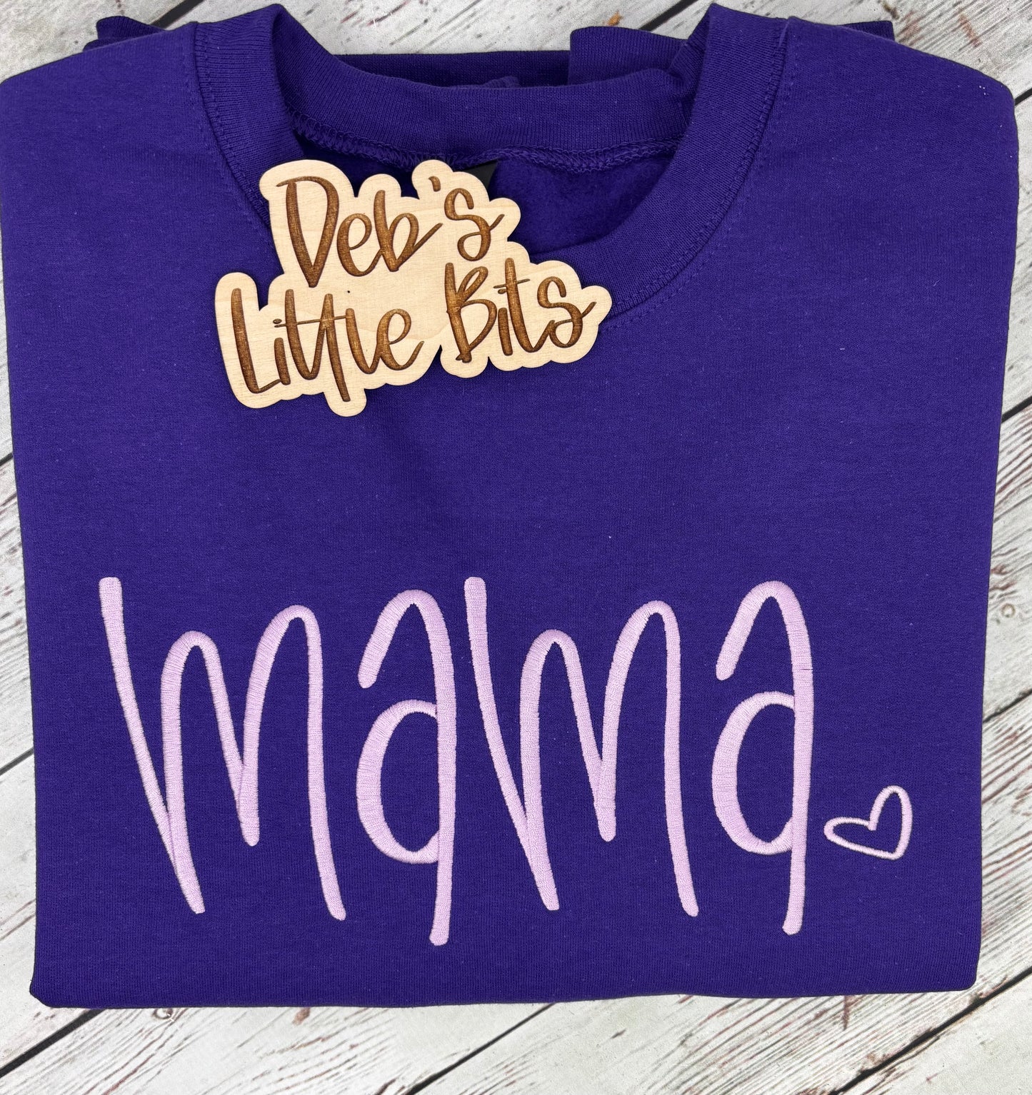 Purple shirt with 'mama' text and wooden cutout on a wooden surface